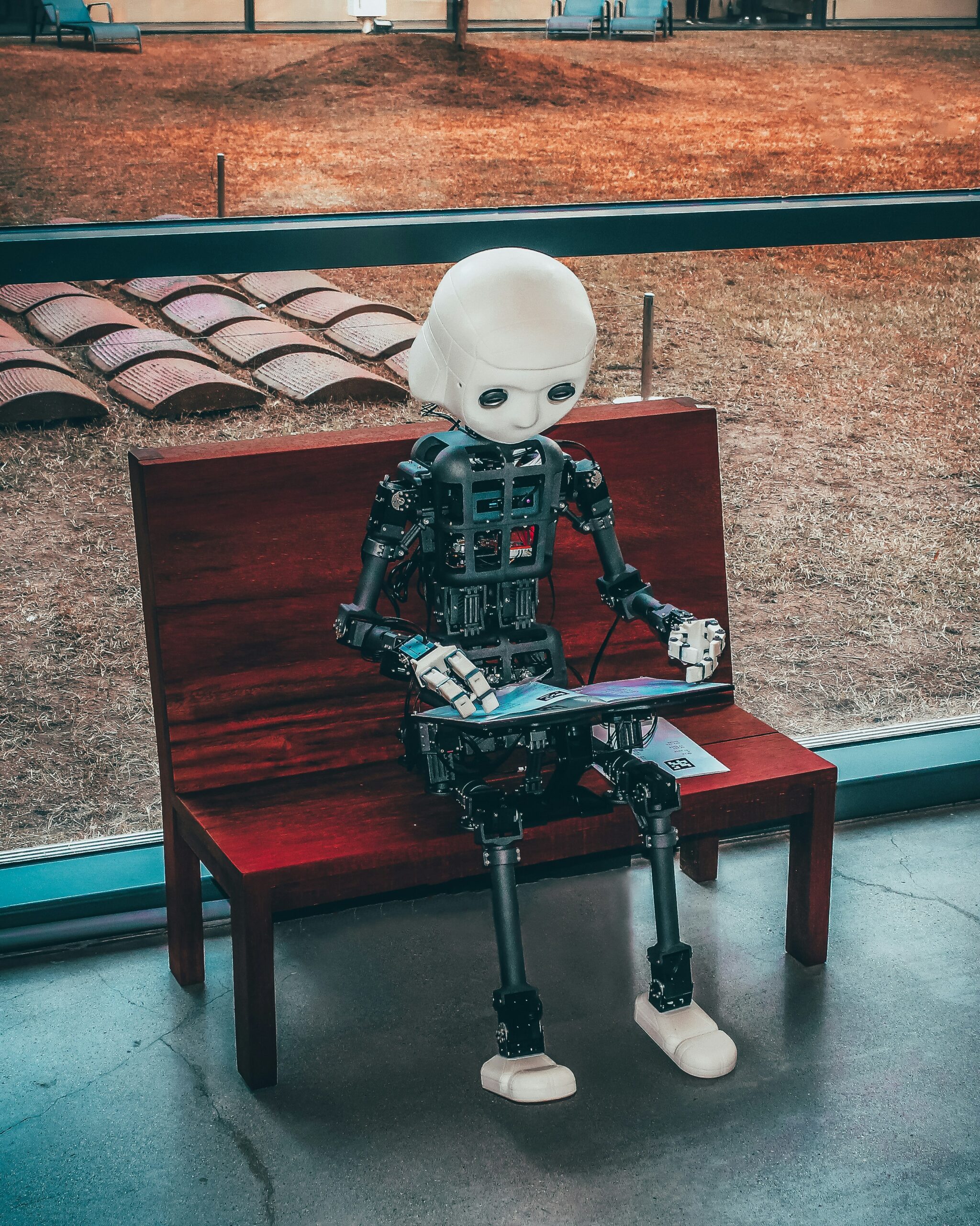 robot in de gedaante van een kind leest een boek op een bankje bewustzijn AI kunstmatige intelligentie